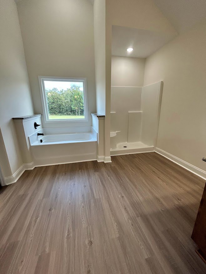 Bathroom featuring a freestanding tub, wood flooring, plaster walls, and a window overlooking trees
