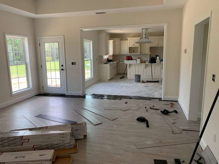 Open kitchen with white cabinetry, wood plank flooring, glass-paneled door, large window overlooking green lawn, and plaster walls