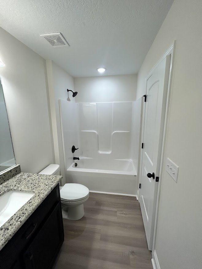 Bathroom with white toilet and seat down, white sink set in black speckled marble countertop, light tile walls, chrome faucet, and minimal accessories.