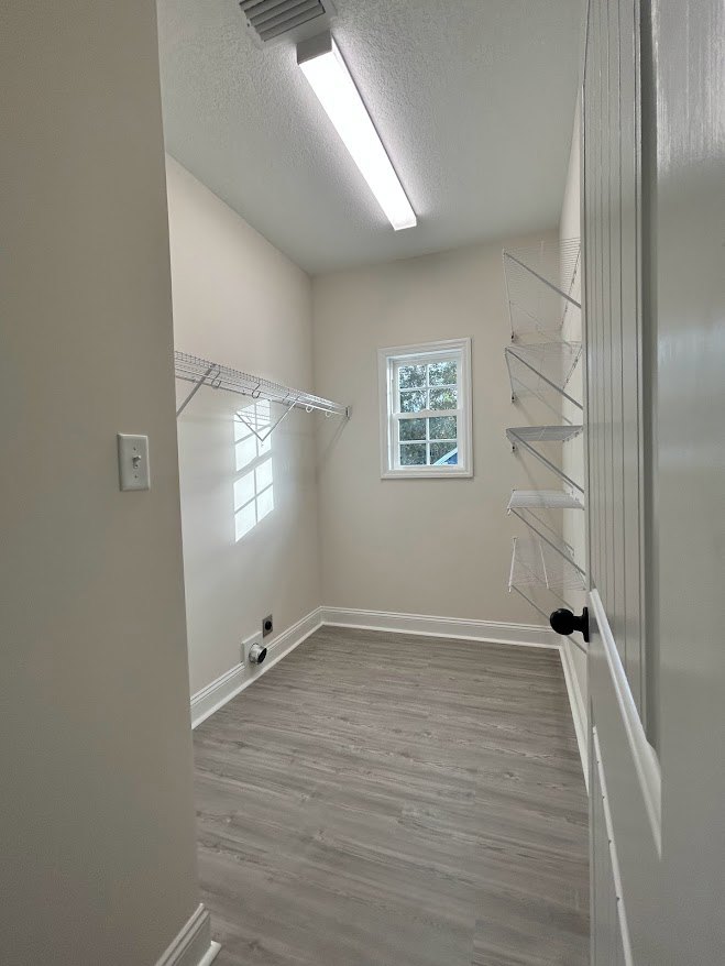 Built-in metal shelves with hooks mounted on a plaster wall, large white-framed window, wood flooring with white baseboard trim, ceiling light fixture