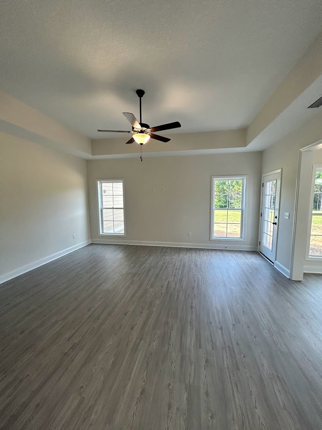 Ceiling fan with light fixture, wood flooring, white walls, window with white frame overlooking grassy yard, white door with black handles