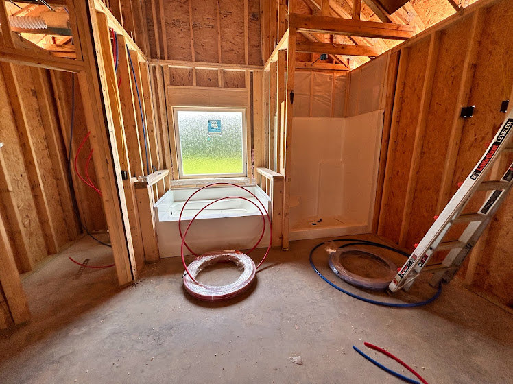 Bathroom under construction featuring exposed insulation, unfinished walls, a white bathtub, aluminum ladder, and bare flooring.