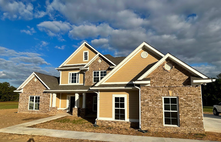 Two-story house with minimal windows, light-colored siding, gabled roof, and small front porch under partly cloudy sky