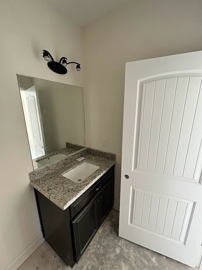 White tile bathroom with rectangular mirror above a white sink, black and white light fixture, light wood cabinetry, and tiled floor.