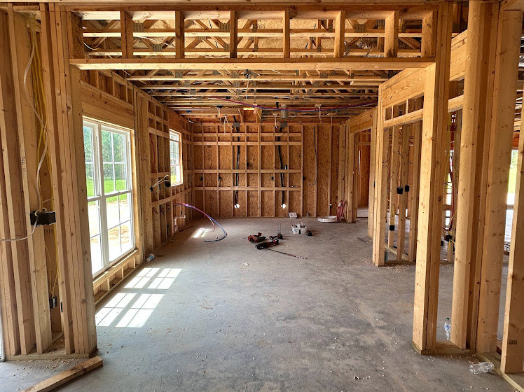 Spacious room featuring a wall of tall windows, exposed wooden beams, unfinished plank flooring, and construction tools scattered on the ground.