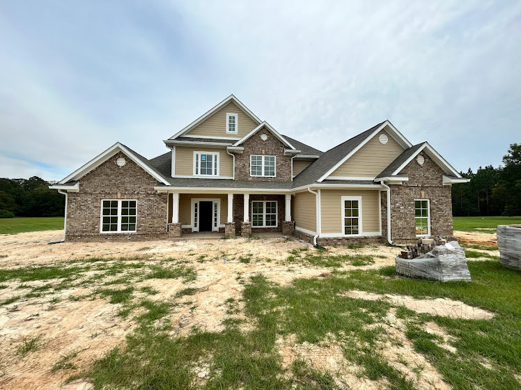 Two-story home with multi-pane windows, wide front porch, gabled roof, expansive grassy yard, and blue sky overhead