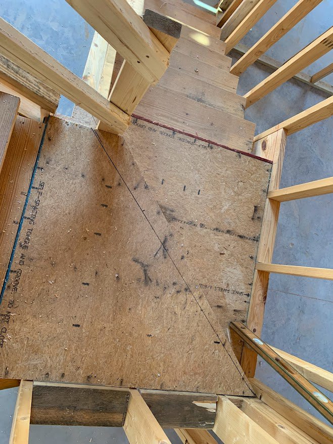 Wooden staircase with matching wood plank flooring, exposed ceiling beams, and unfinished wooden framing along the wall.