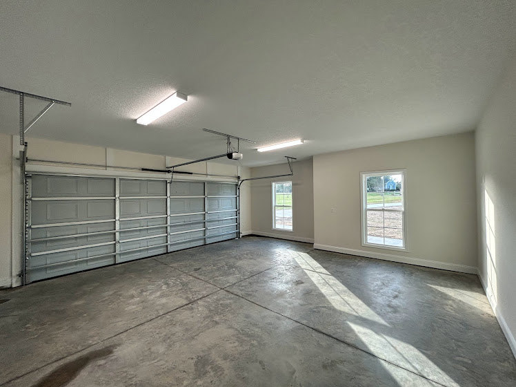 Spacious garage with smooth concrete floor, white plaster walls, and ceiling, illuminated by overhead fixtures