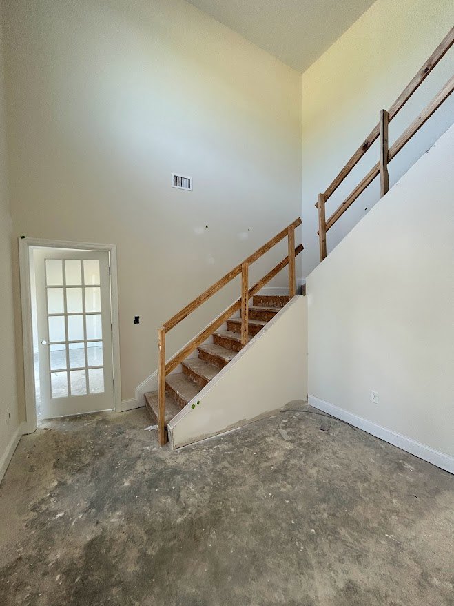 Wood staircase with wooden railing, concrete floor, white door with glass panes, plaster walls, and ceiling in a residential interior.