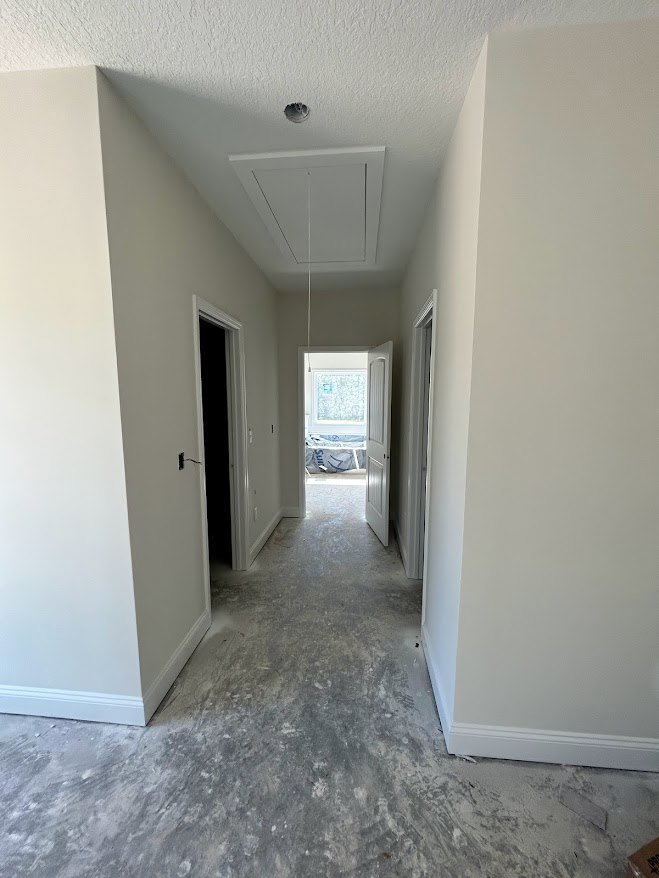 Hallway with white plaster walls and ceiling, open white door leading to a room, ceiling vent, light-colored flooring