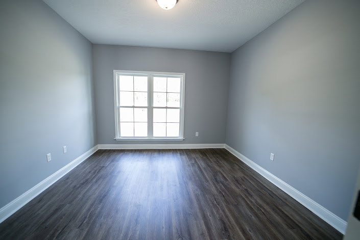 Sunlit room featuring large window, light-colored hardwood flooring, white plaster walls, and minimalist interior design.