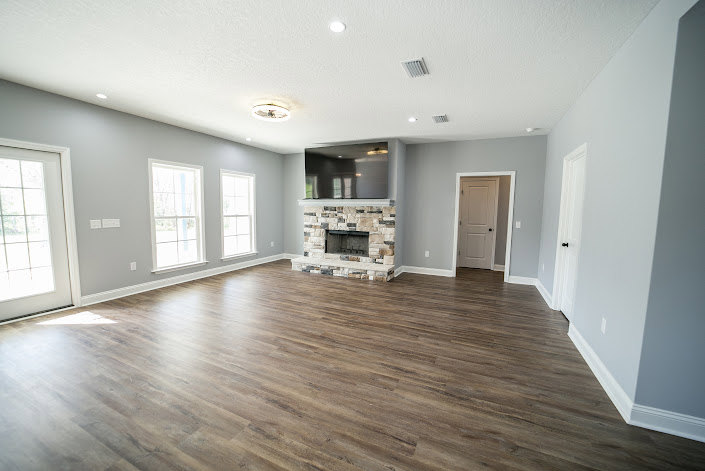 Living room featuring a stone fireplace, hardwood floors, white walls, and recessed ceiling lighting