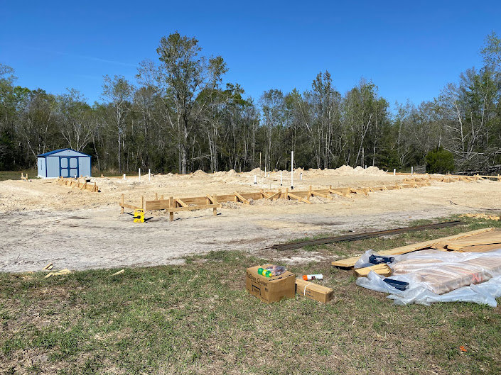 Building site with grassy ground, blue shed, scattered trees, and open sky