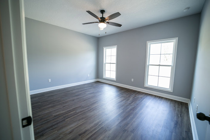 Ceiling fan mounted above laminate wood flooring, plaster walls, and large windows in a bright residential interior.