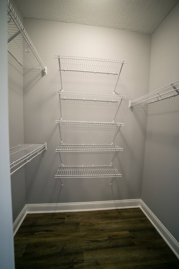 Closet with white built-in shelves, white ladder leaning against wall, dark wood floor, and white baseboards