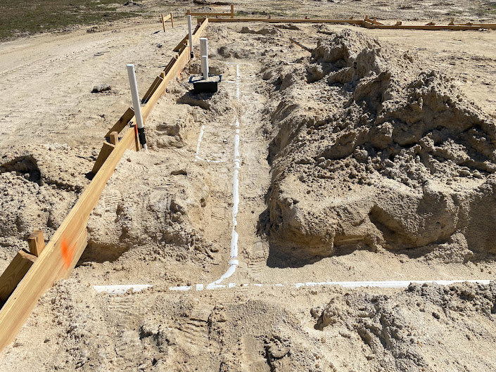 Trench dug into soil at residential construction site with exposed white pipes and scattered rocks