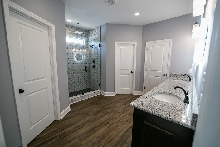 Bathroom featuring marble countertop, undermount sink, glass-enclosed shower with tile walls, light wood cabinetry, and neutral tile flooring