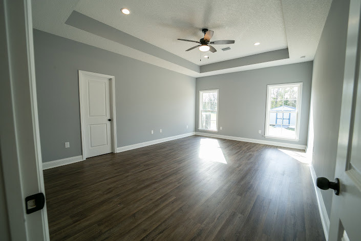 Living room with laminate wood flooring, plaster walls, ceiling fan, and large windows letting in natural light.