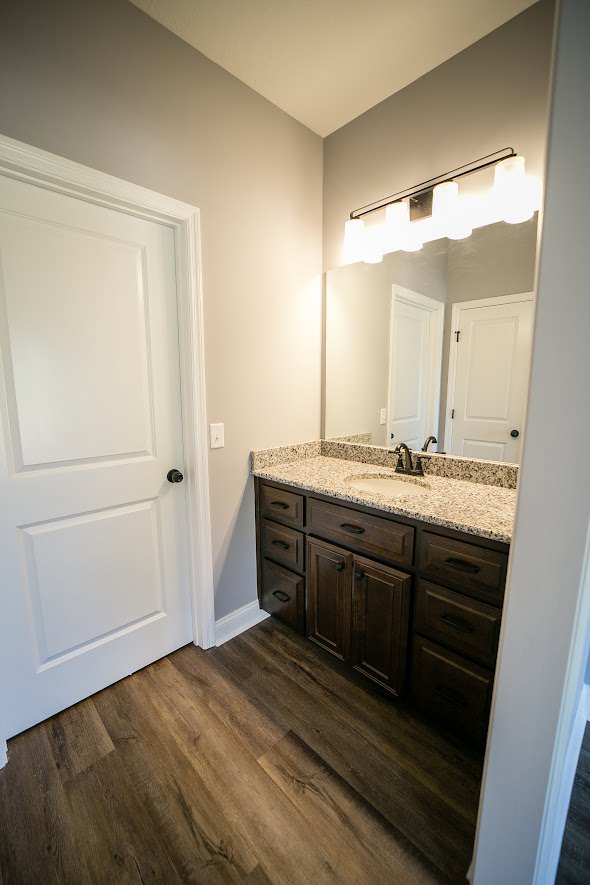 Bathroom with marble countertop, rectangular mirror above sink, white cabinetry, black door knob on white door, light tile flooring