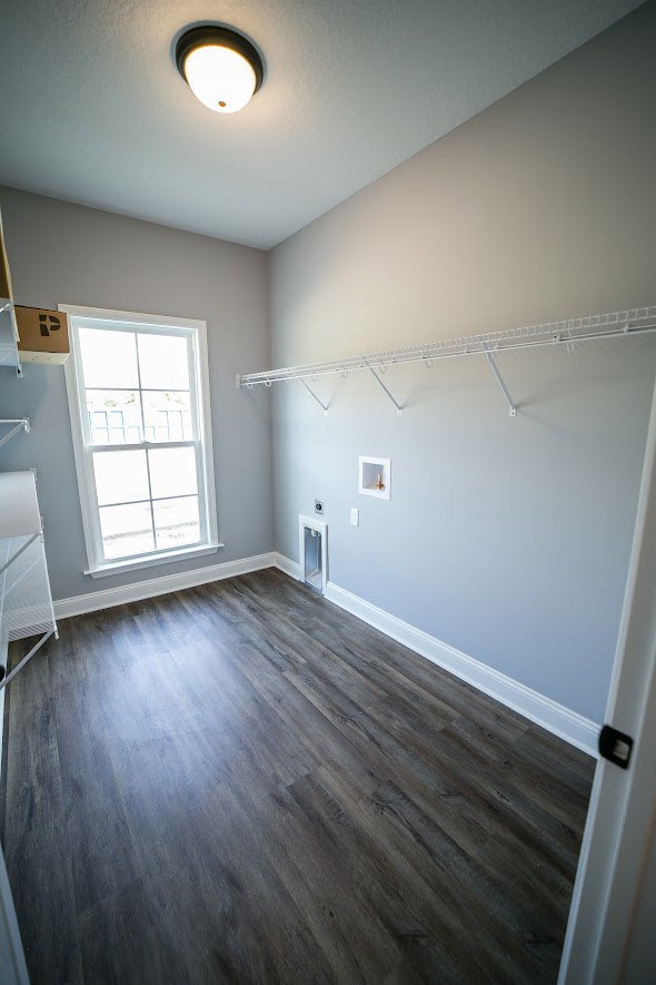 Wood flooring in a room with plaster walls, large window with white frame, and white metal rack with hooks