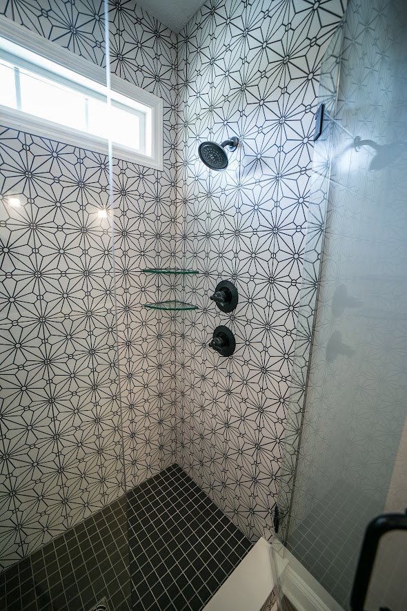 Shower with black and white geometric tile walls and floor, round chrome shower head, shadow cast on white tile, partial view of bathroom fixtures