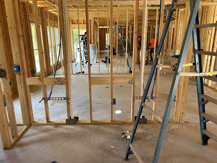 Unfinished room with exposed wood beams, construction insulation, and multiple ladders positioned in the center on a bare floor