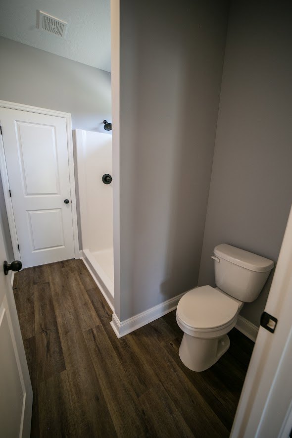 White tile bathroom featuring a modern toilet, glass-enclosed shower, and light gray flooring