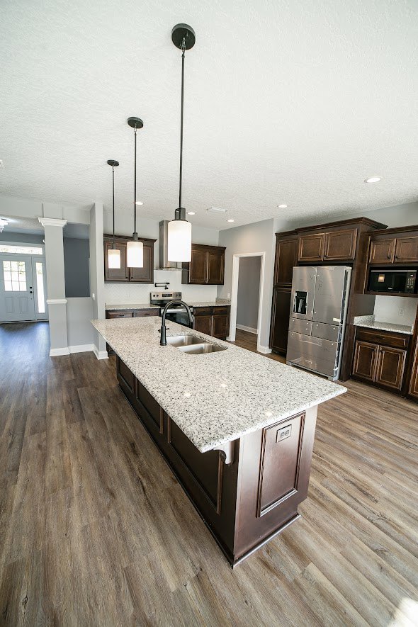 Spacious kitchen featuring a large central island with white quartz countertop, open stainless steel refrigerator, light wood cabinetry, and wide plank flooring.