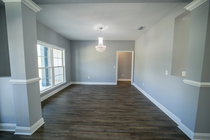 Wood plank flooring, ornate chandelier, white plaster walls with crown molding, high ceiling, open interior space