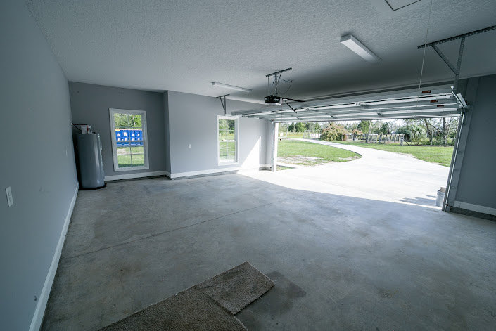 Spacious garage with wide sectional door, smooth concrete flooring, white plaster walls, and ceiling-mounted lighting fixtures