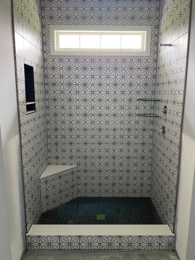 Walk-in shower featuring a tiled wall with gray and white ceramic tiles, glass enclosure, and chrome plumbing fixtures; window provides natural light.