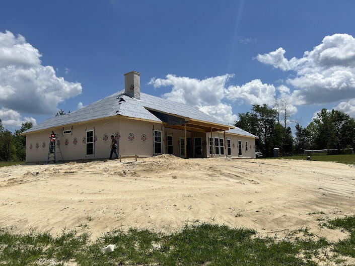 Modern house with central two-story structure, surrounded by manicured lawn, mature trees, and expansive windows under a partly cloudy sky