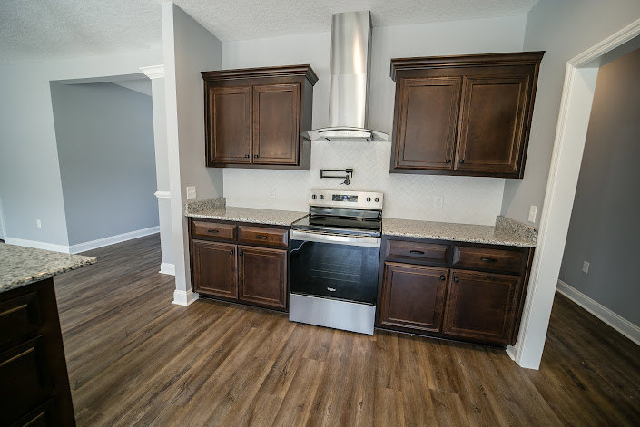 Kitchen with dark wood cabinets, stainless steel stove, stone countertop, and tile flooring