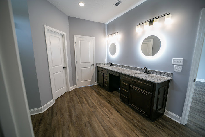 Bathroom featuring a double vanity with white countertop, two round mirrors above each sink, light wood cabinetry, tile flooring, and neutral wall finishes.