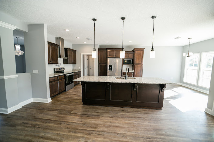Spacious kitchen featuring a large central island with stone countertop, white cabinetry, stainless steel microwave and stove, tile backsplash, undermount sink, and hardwood