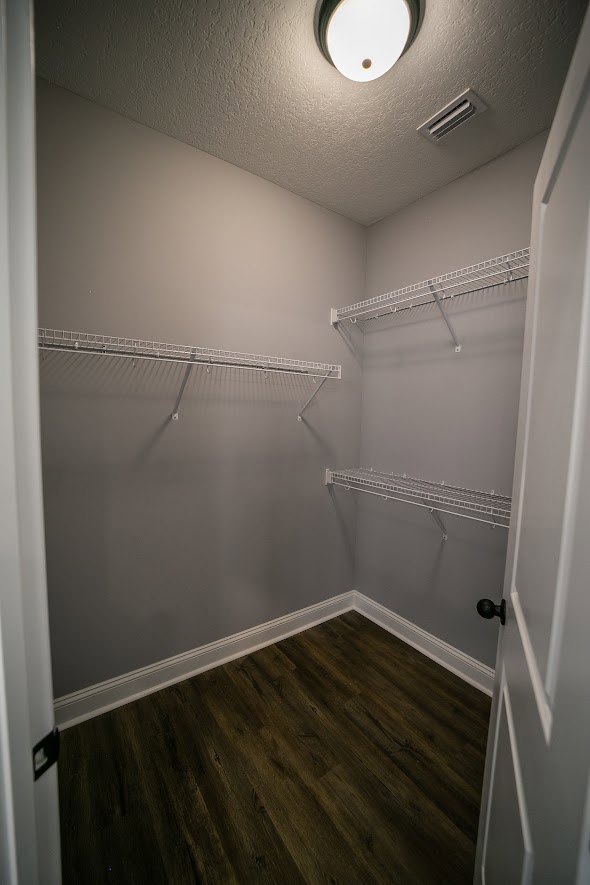 Walk-in closet with white shelving, wood plank flooring, white walls, and a white door with black hardware