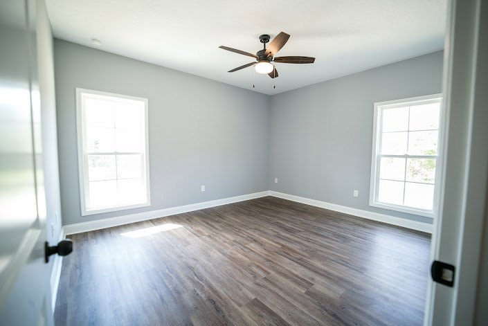 Ceiling fan with light fixture mounted on white plaster ceiling, hardwood flooring, large windows with natural light, neutral painted walls