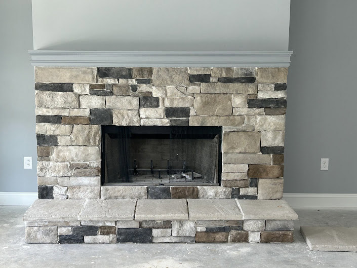 Stone fireplace with hearth, fire screen, and wood mantel shelf in a residential living room