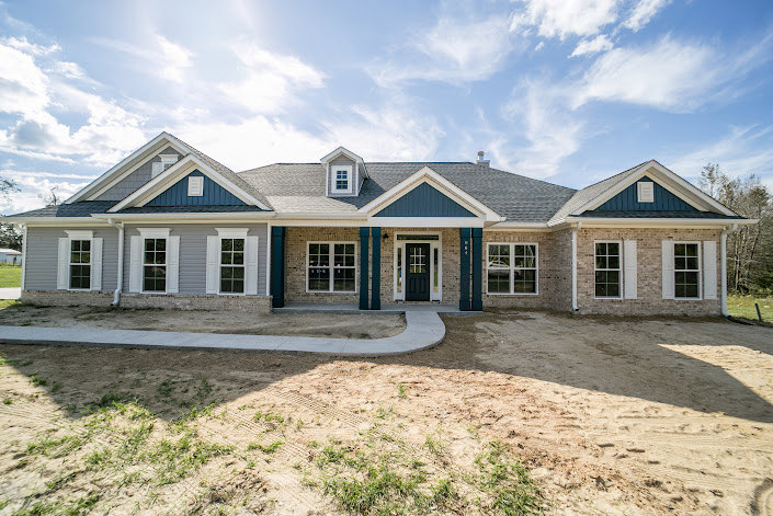 Blue and white two-story home with large windows, covered front porch, paved driveway, manicured lawn, and partly cloudy sky overhead