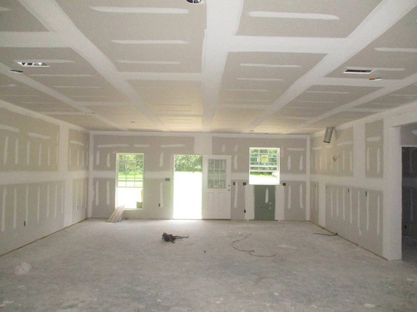 White-walled room with a white ceiling, metal-barred window framed by green leaves, and a cat resting on the light-colored floor