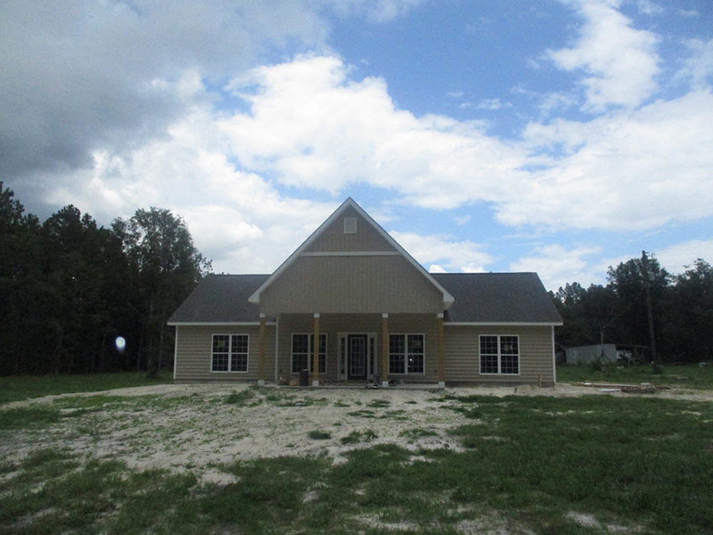 Two-story house with a triangular roof, white multi-pane windows, and a spacious grassy front yard surrounded by mature trees.