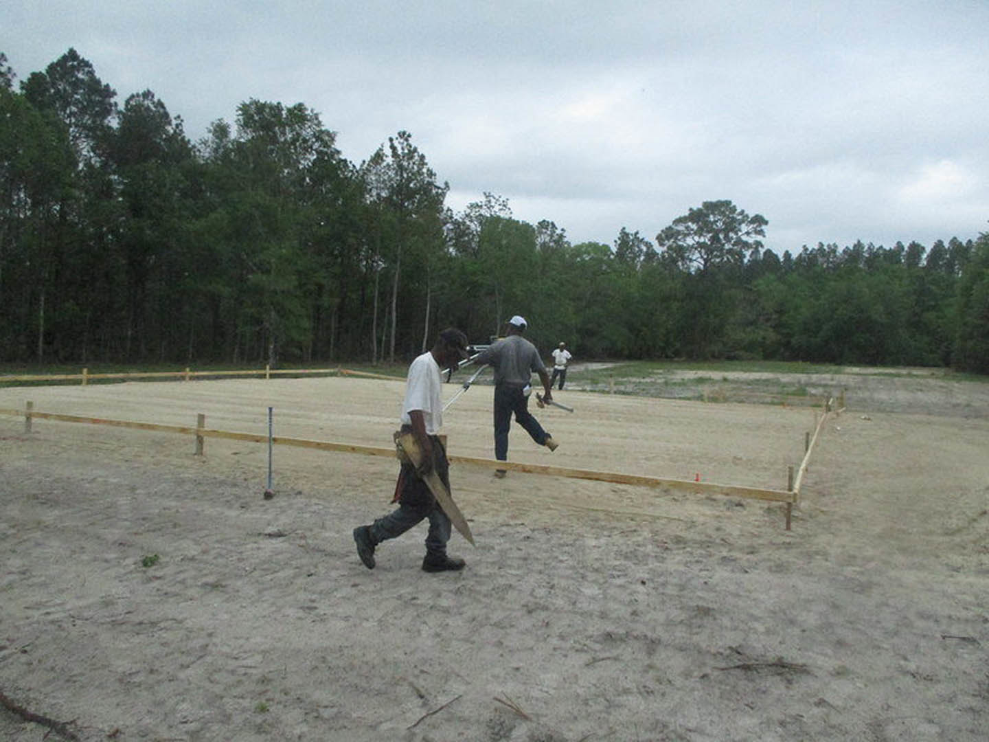 Modern custom home exterior with light stone facade, large windows, manicured lawn, and mature trees under partly cloudy sky