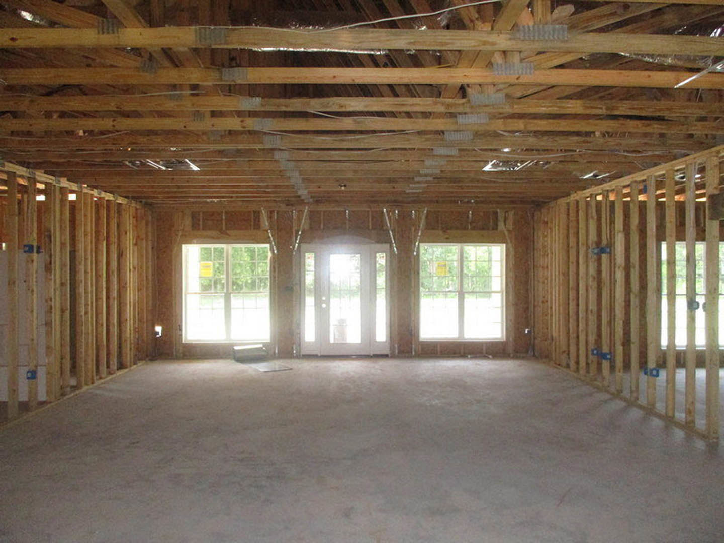 Wood-beamed ceiling with exposed insulation, white door with glass panes, large windows, light wood flooring, yellow sign visible on window