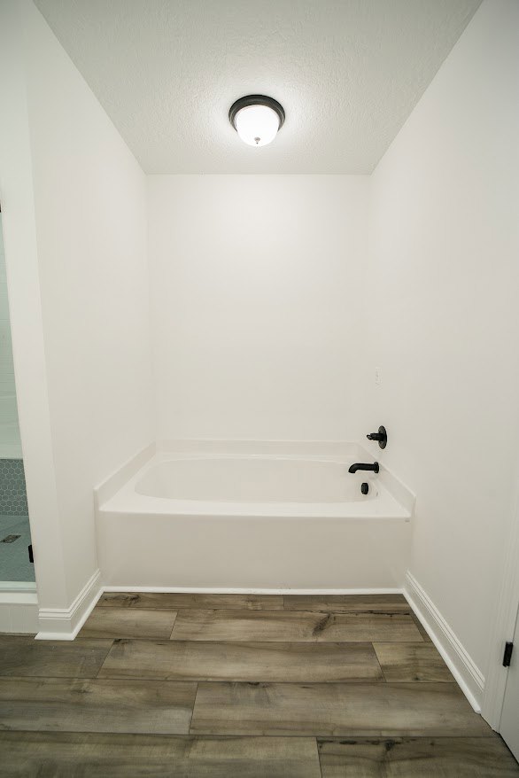 Freestanding white bathtub with marble tile surround and plaster walls in a modern bathroom