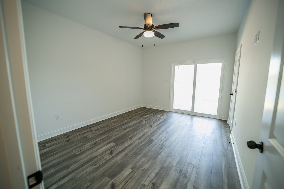 Ceiling fan with light fixture, white framed window, wood laminate flooring, white door, plaster walls