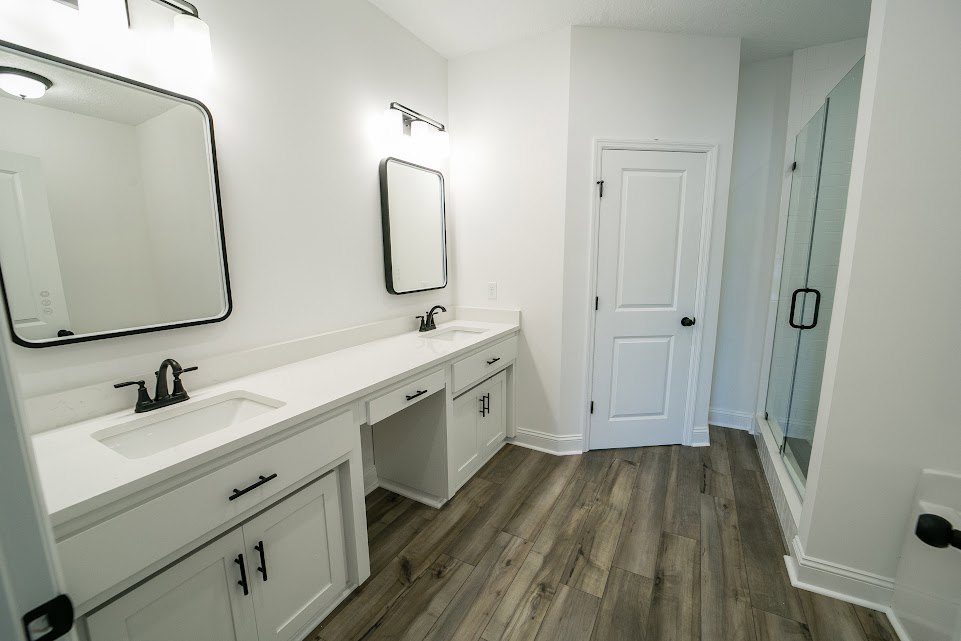 Bathroom with white shaker cabinets, black hardware, white countertop featuring a long black faucet, wall-mounted mirror with integrated lighting, and tile flooring.