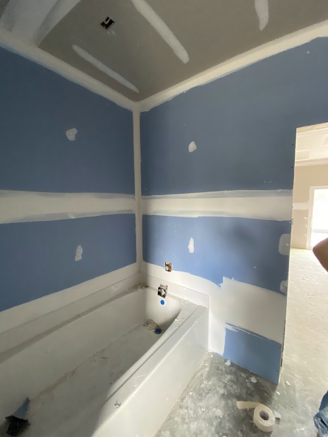 Bathroom featuring blue and white striped tile walls, white bathtub with blue roller, roll of toilet paper on holder, sunlight illuminating white plaster wall, close-up of smooth