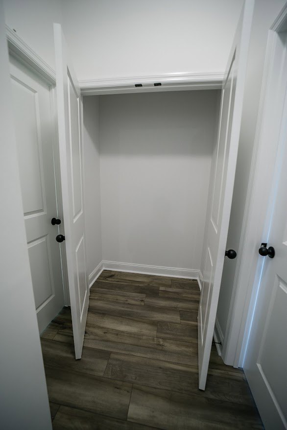 Closet with white walls, wood floor, black door, white trim, and black door knobs