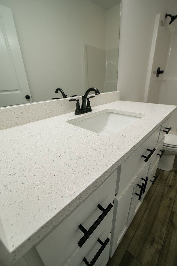 White bathroom featuring a rectangular sink with chrome faucet, large frameless mirror above, white tile walls, and a glimpse of a white bathtub in the background.