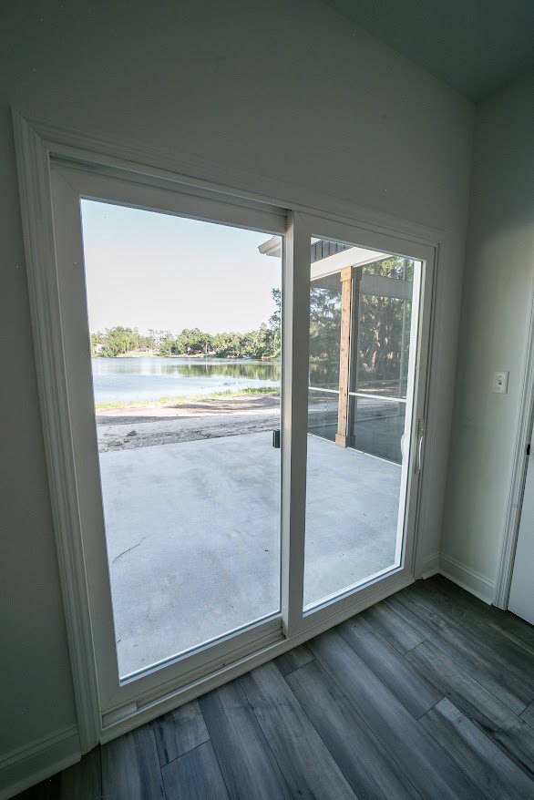 Sliding glass door with lake and tree views, wooden floor, wood post, white walls